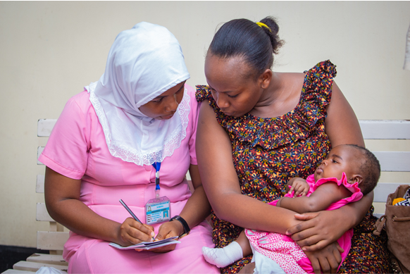 Nursing student wearing pink working with a mother and child. 